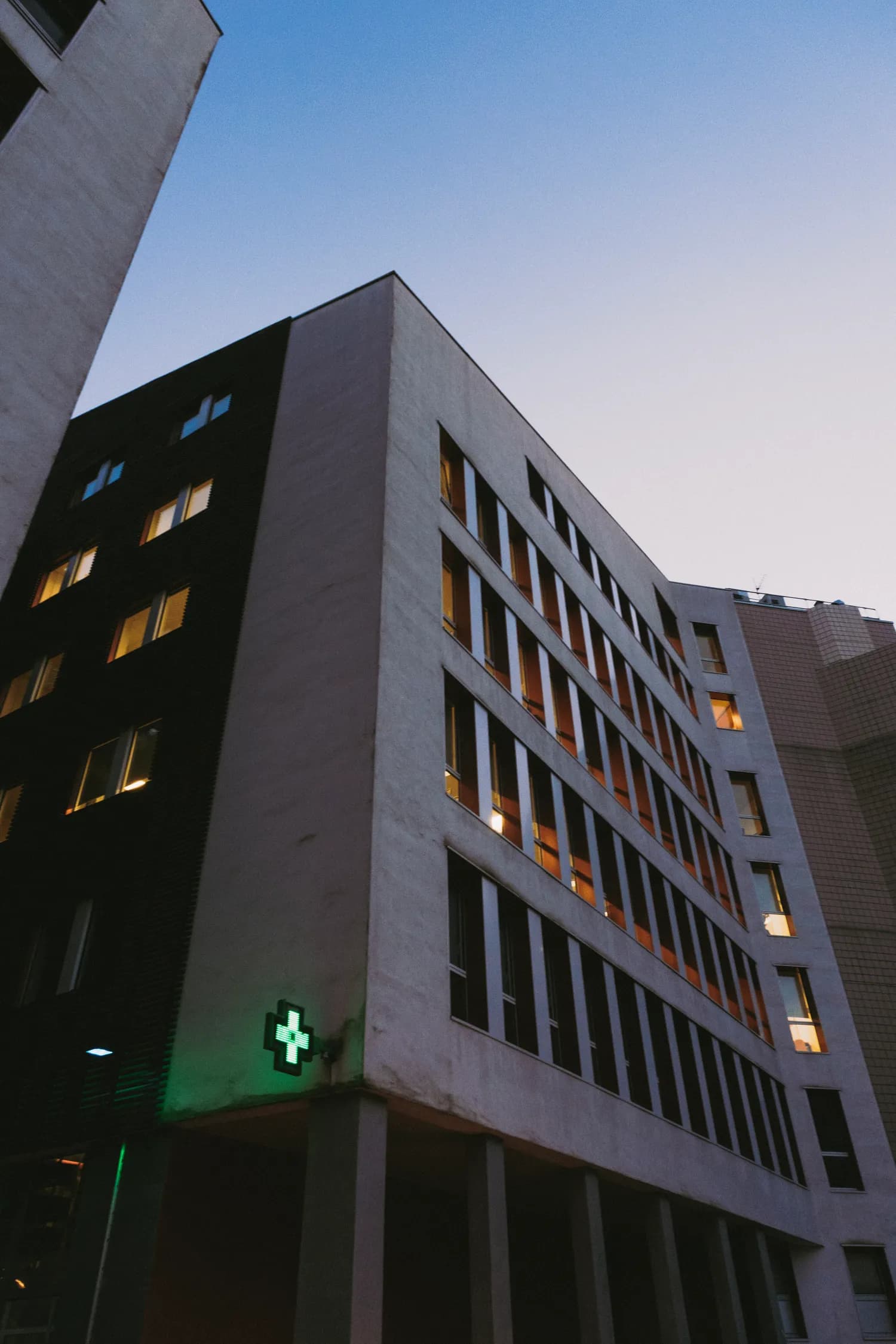 A modern hospital building exterior with a green cross